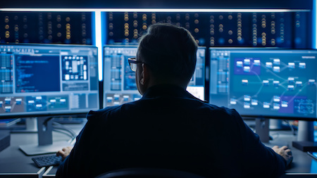 cybersecurity professional looking at three computer monitors